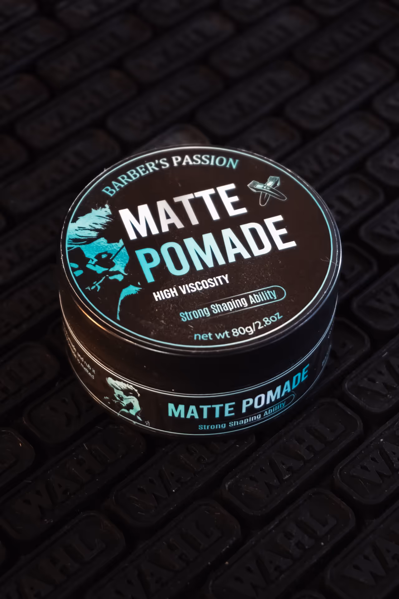 Round black container of matte pomade with teal and white text reading 'Barber's Passion Matte Pomade, High Viscosity, Strong Shaping Ability, net wt 80g/2.8oz' on a textured black surface.
