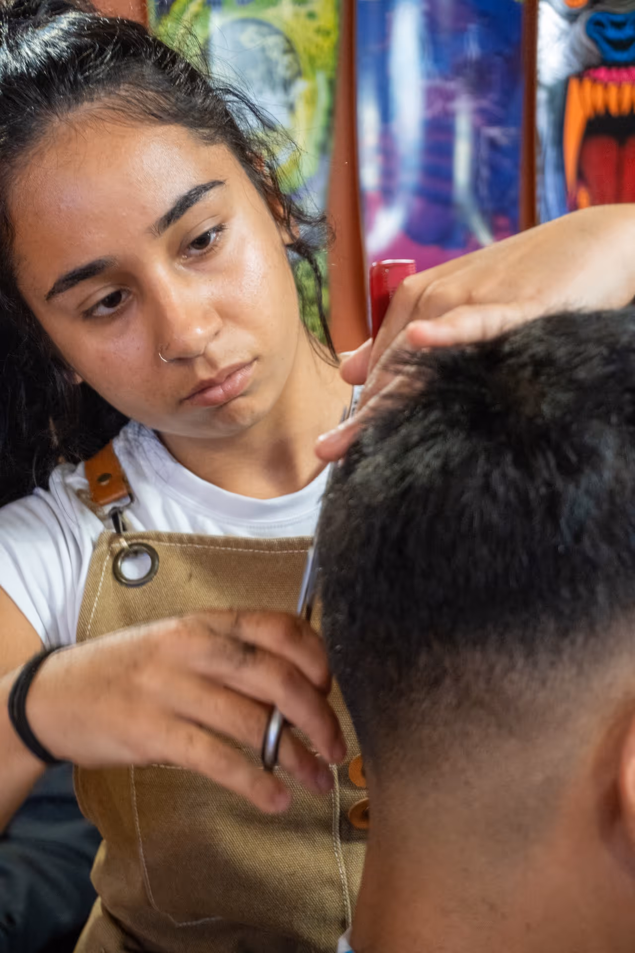 Barber wearing a brown apron styling a client's short hair with clippers.