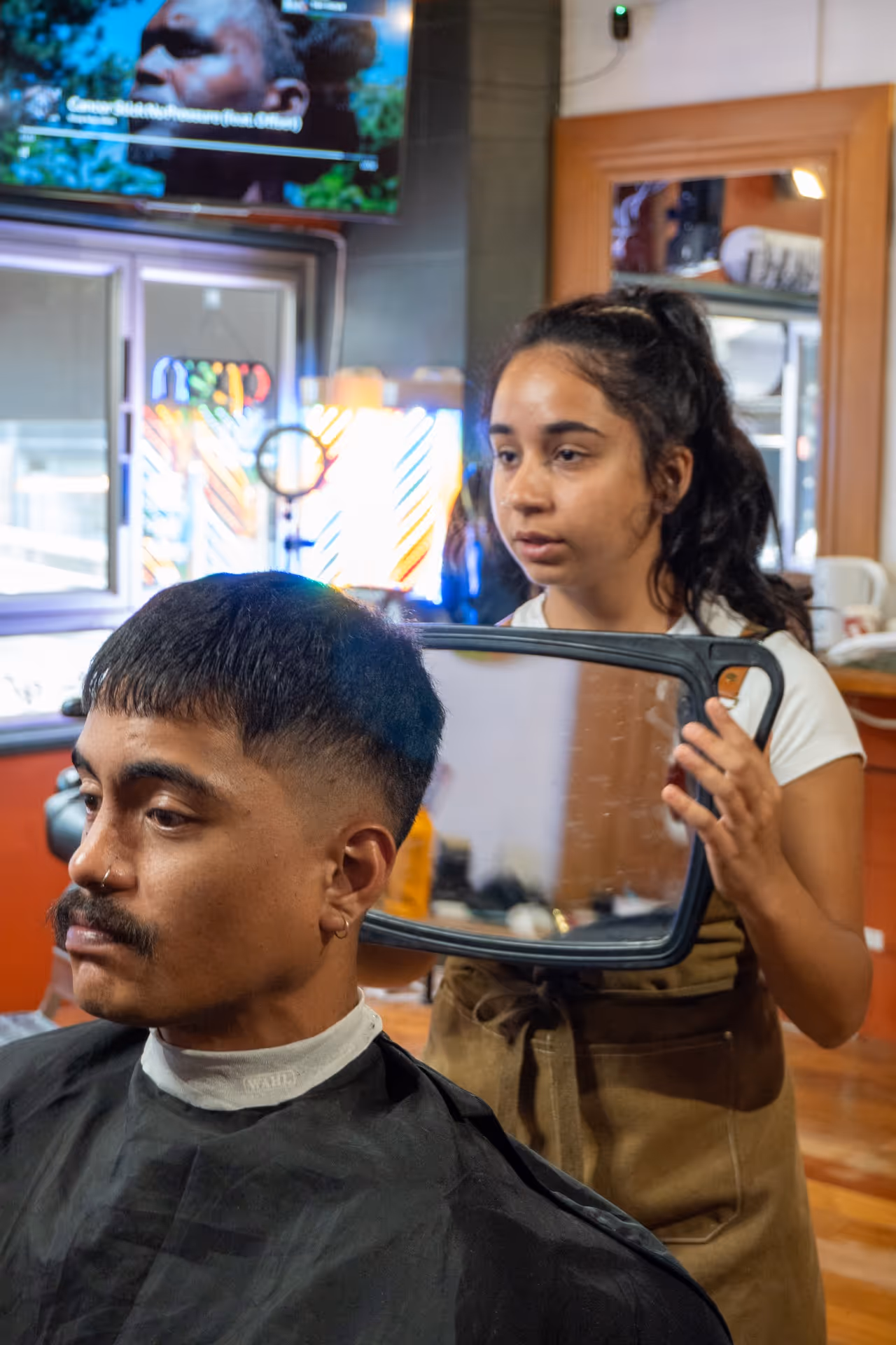 Barber holding a handheld mirror to show a man his fresh haircut in a barbershop.