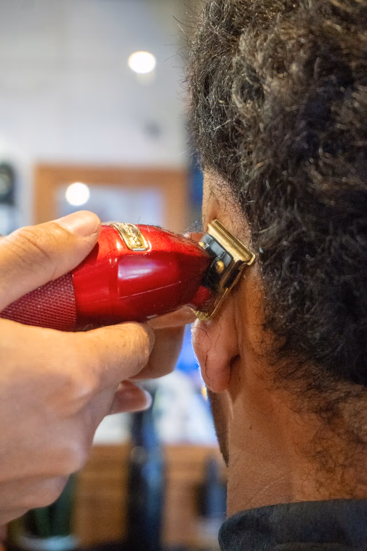 Close-up of a barber using a red electric trimmer to cut hair near a person's ear.