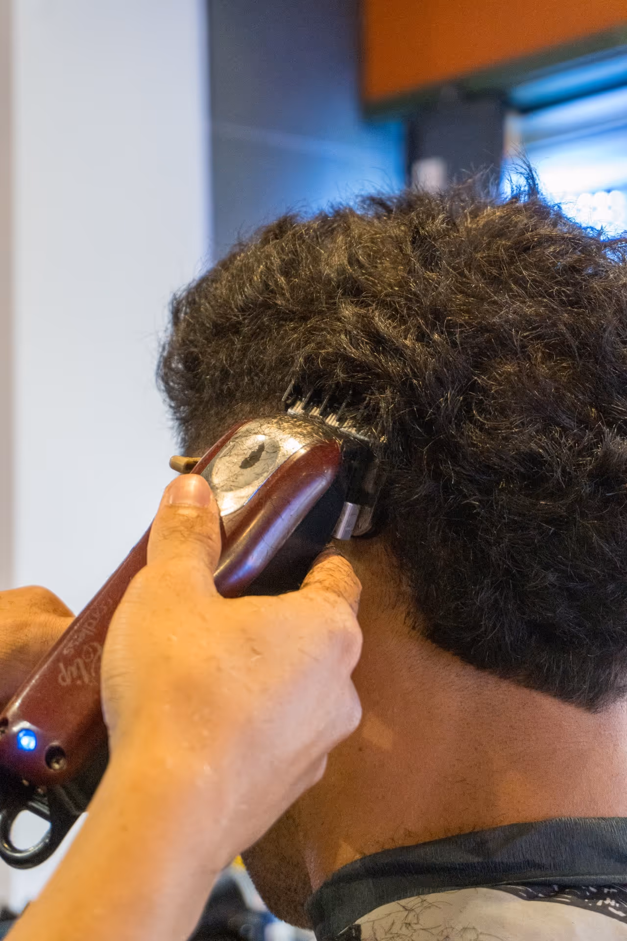 Close-up of a barber using electric clippers to trim a man's curly hair at the back of his head.